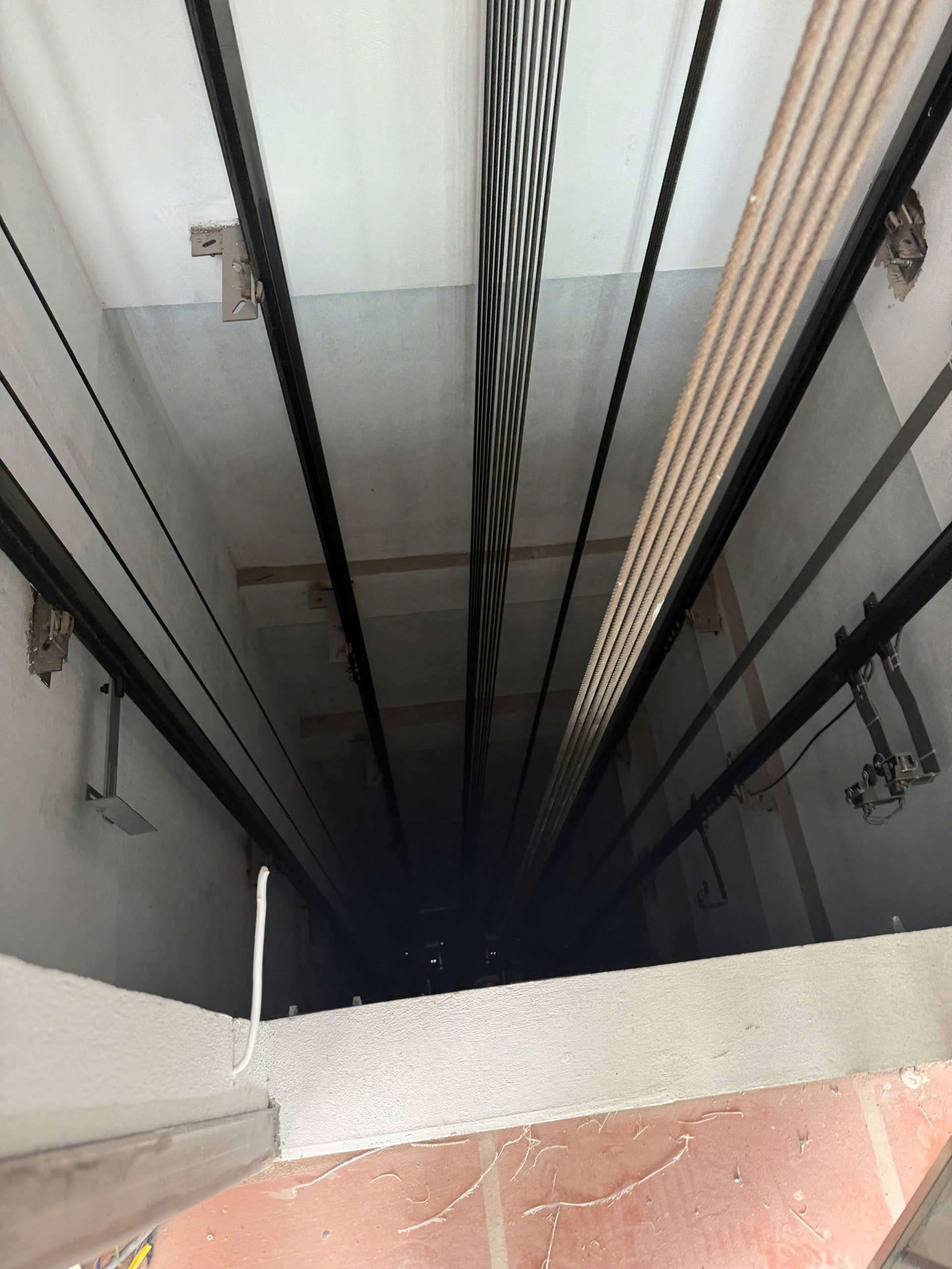 Hố thang máy đang thi công với hệ thống cáp và ray dẫn hướng nhìn từ trên xuống